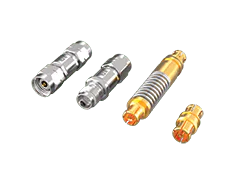 Verschiedene Koaxialstecker aus Metall mit vergoldeten Anschlüssen auf grünem Hintergrund, zur Präsentation diagonal angeordnet.